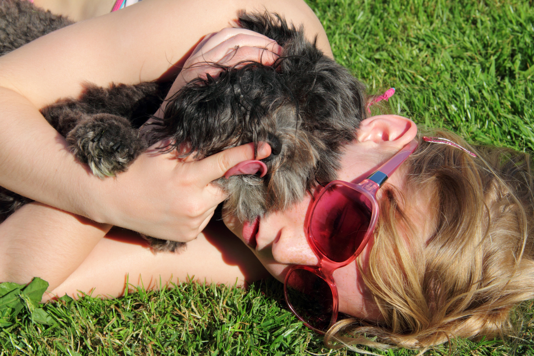Lady lying outdoors on the grass cuddling her pet dog